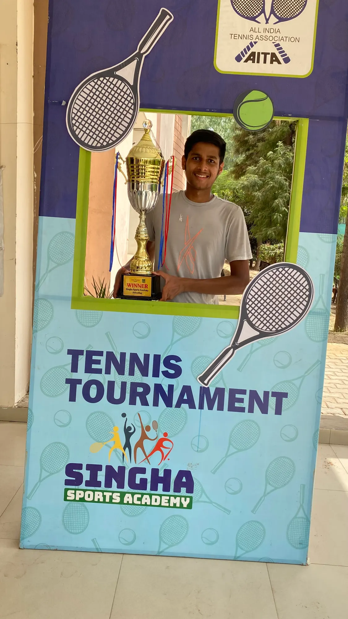 Agrim as a junior holding a winner's trophy in an AITA tournament photo frame