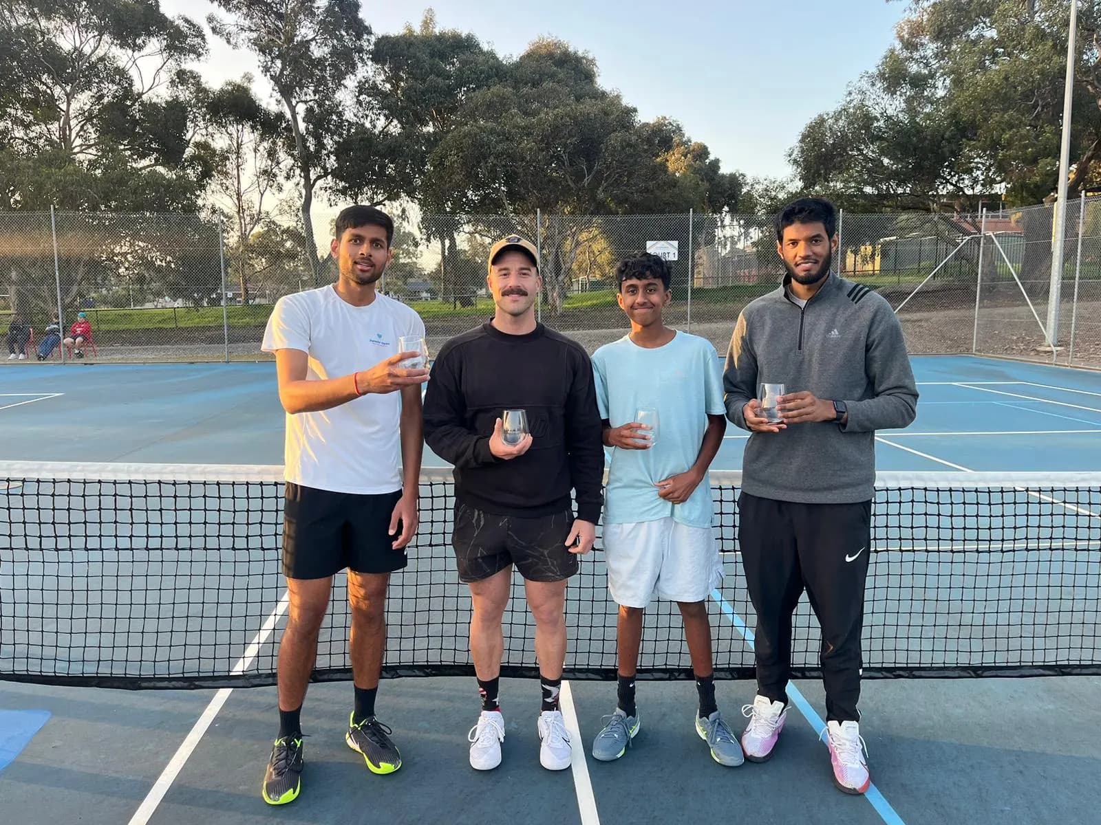 Four players at the net at Tea Tree Gully Tennis Club, each holding a small trophy