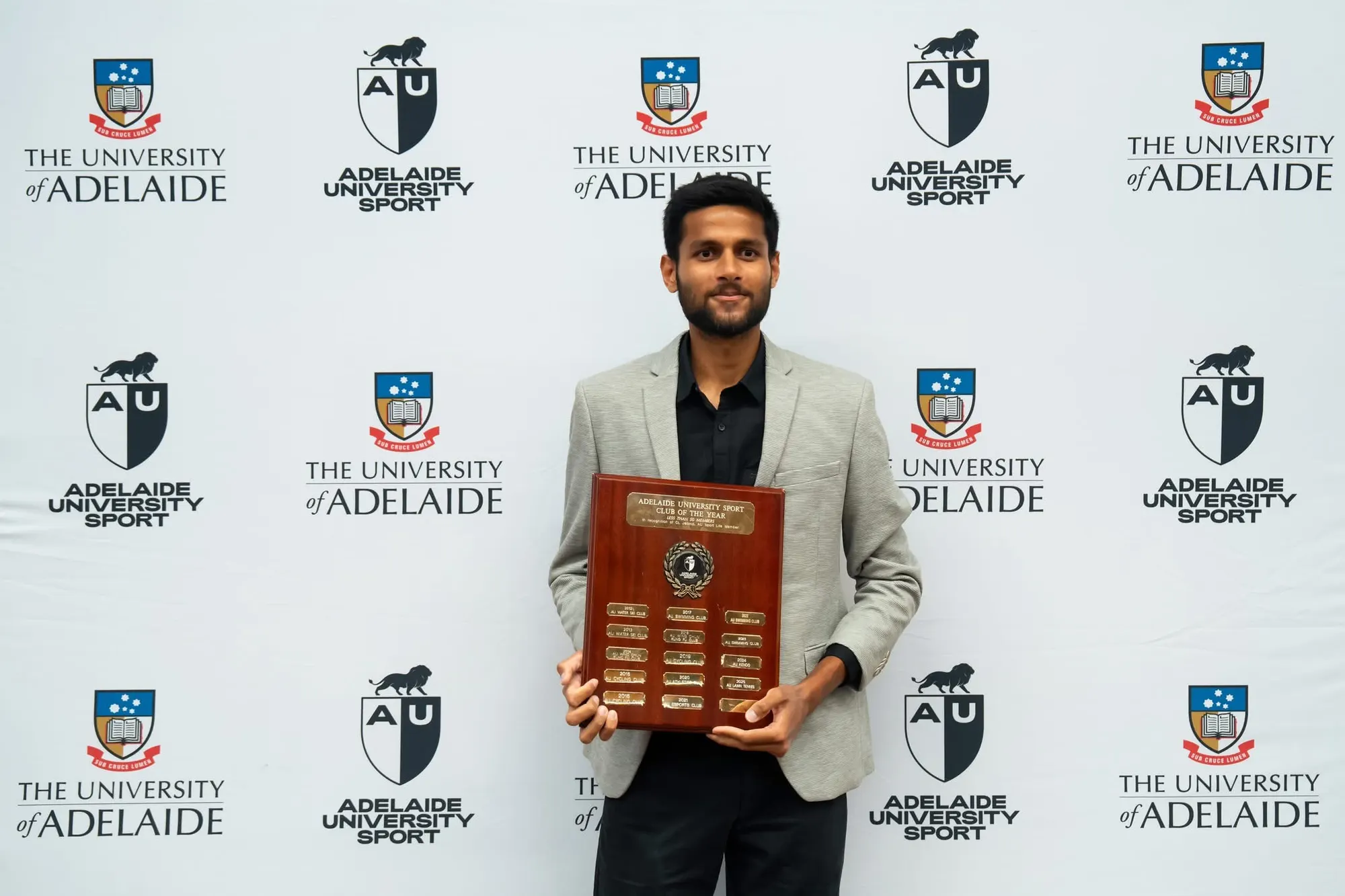 Agrim holding the Club of the Year shield in front of an Adelaide University backdrop